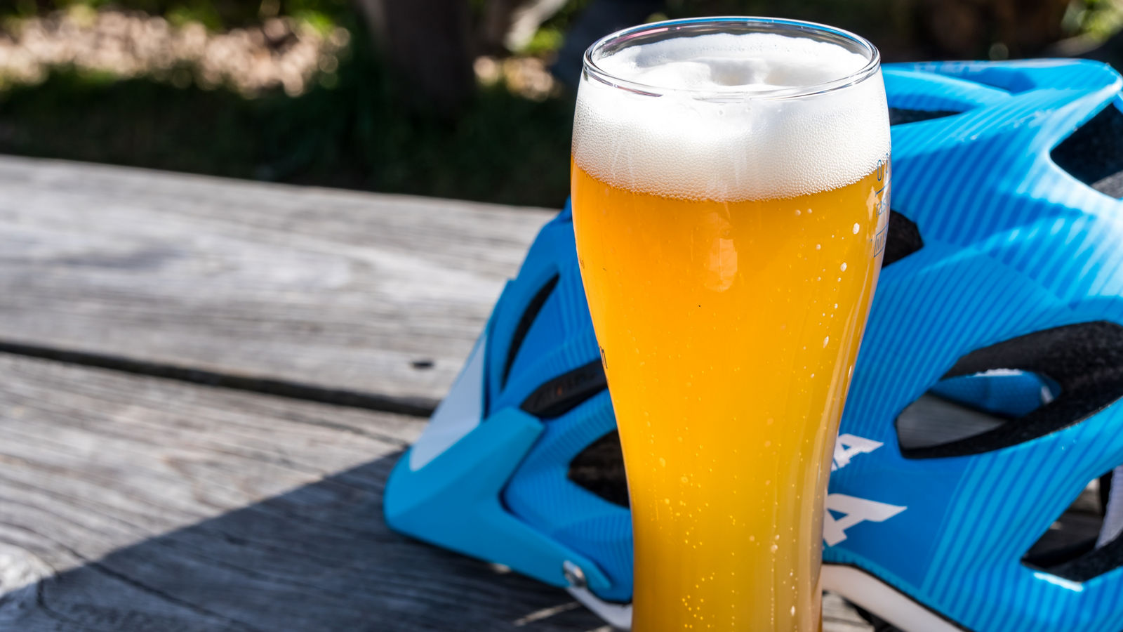 Weizenbier und blauer Fahrradhelm auf Holztisch