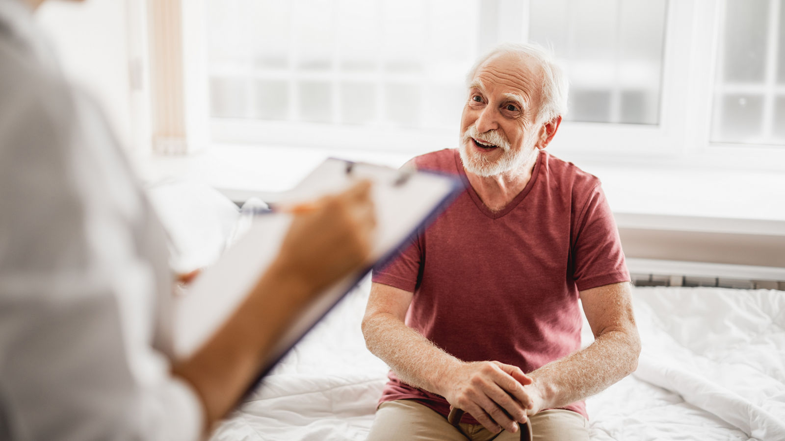 Joyful old man sitting on hospital bed and chatting with doctor