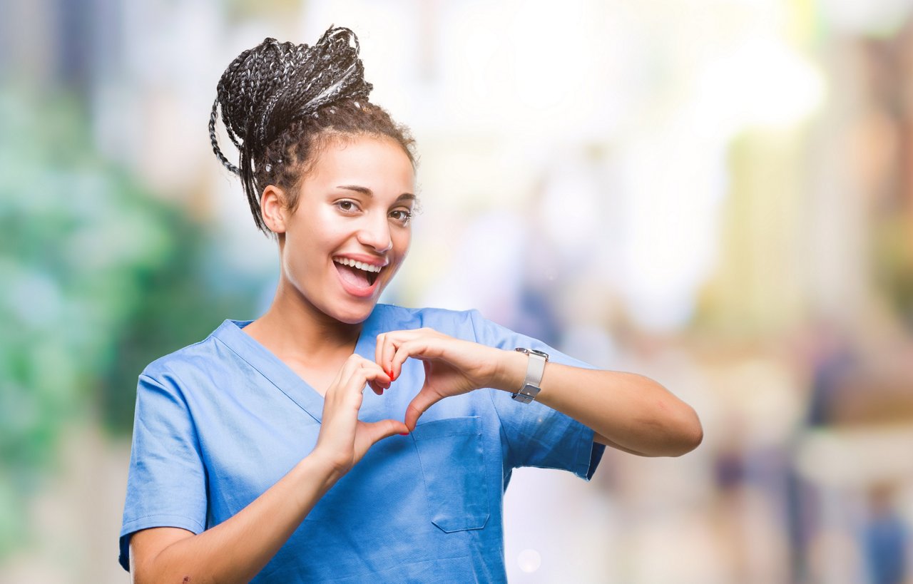 Young braided hair african american girl professional nurse over isolated background smiling in love showing heart symbol and shape with hands. Romantic concept.