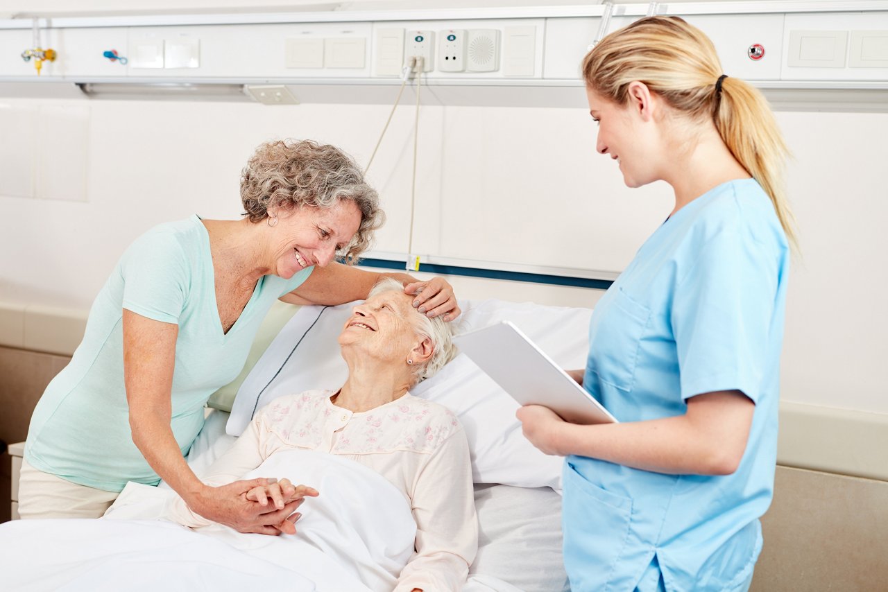 Frau macht Krankenbesuch bei einer Seniorin im Pflegeheim oder Krankenhaus