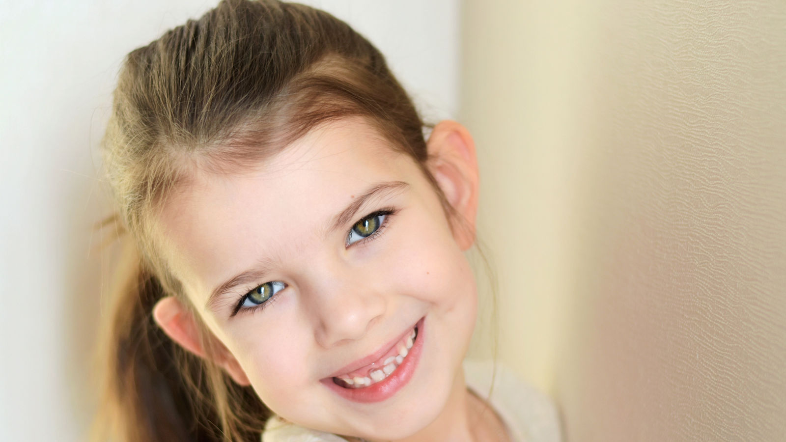 portrait of a little caucasian white beautiful brunette girl with pony tail on neutral background. smiling toothless green eyed happy girl with cute protruding ears. Kid expression portrait with fun h