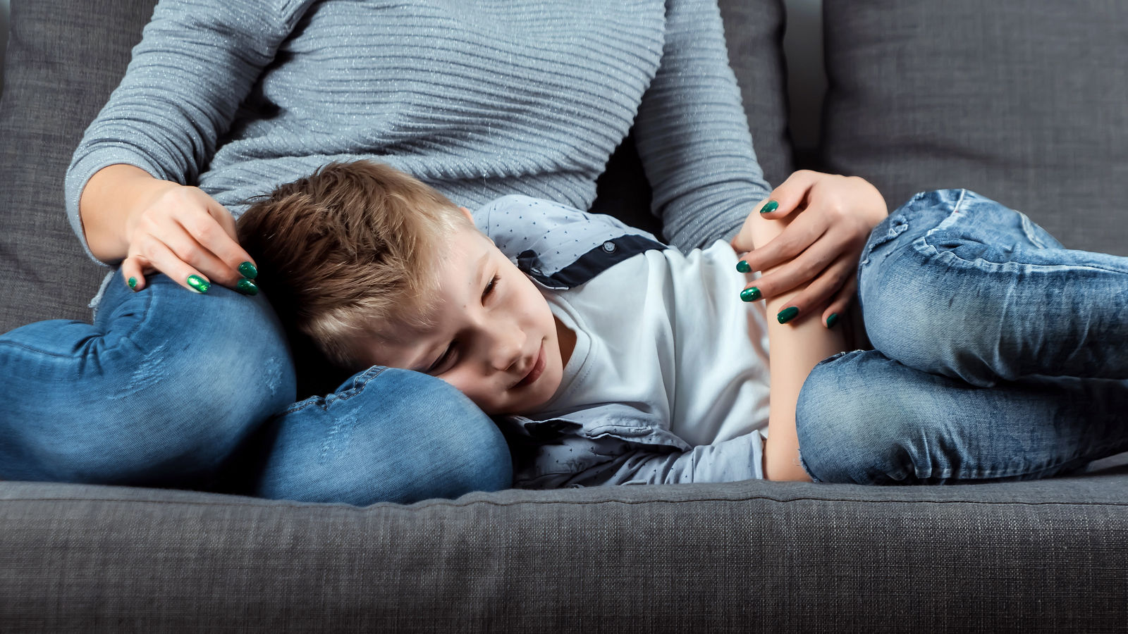 The boy is lying on the couch with an abdominal pain near his mother. The concept of custody, parental care, stomach problems, food poisoning, problems in children.