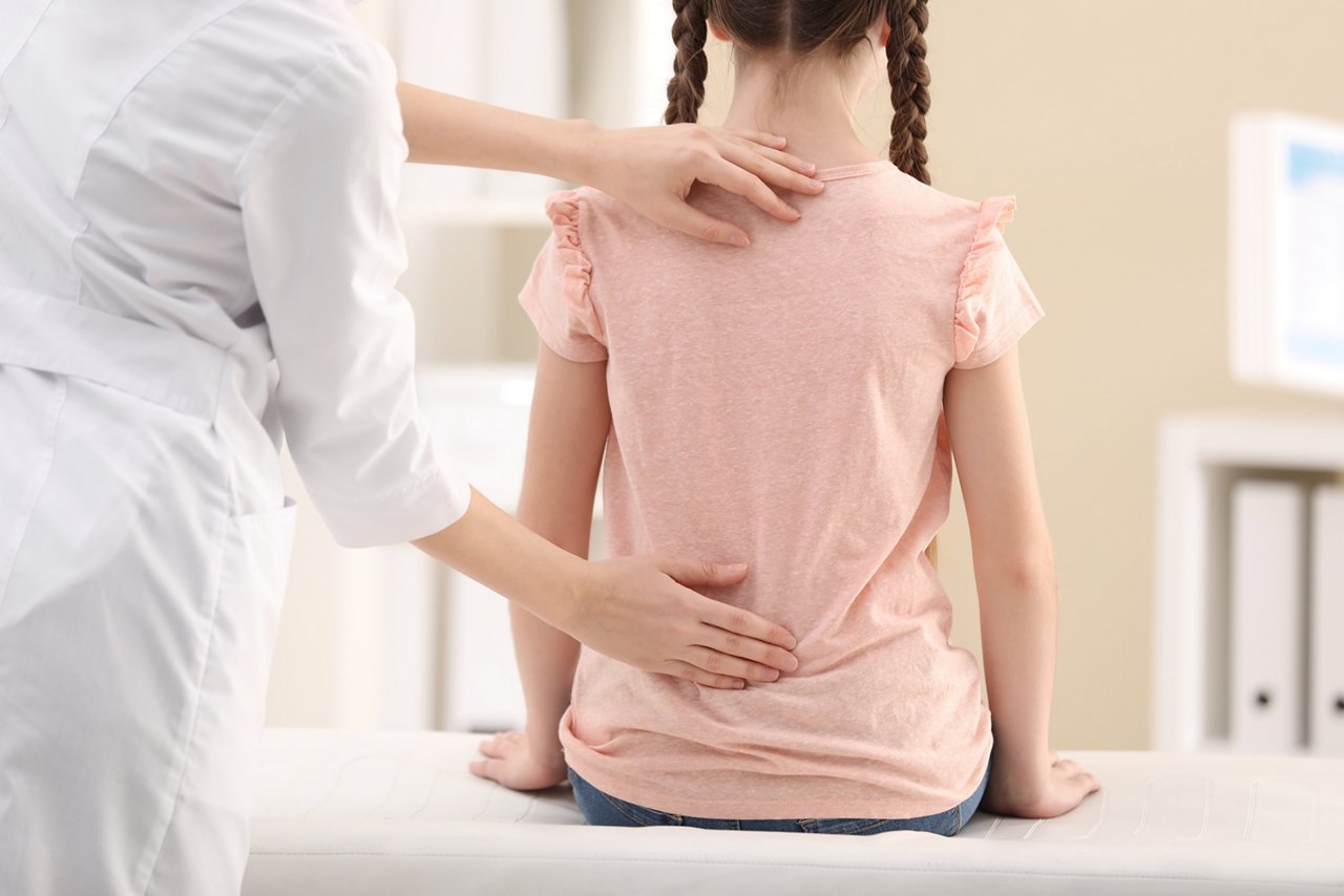 Chiropractor examining child with back pain in clinic, closeup
