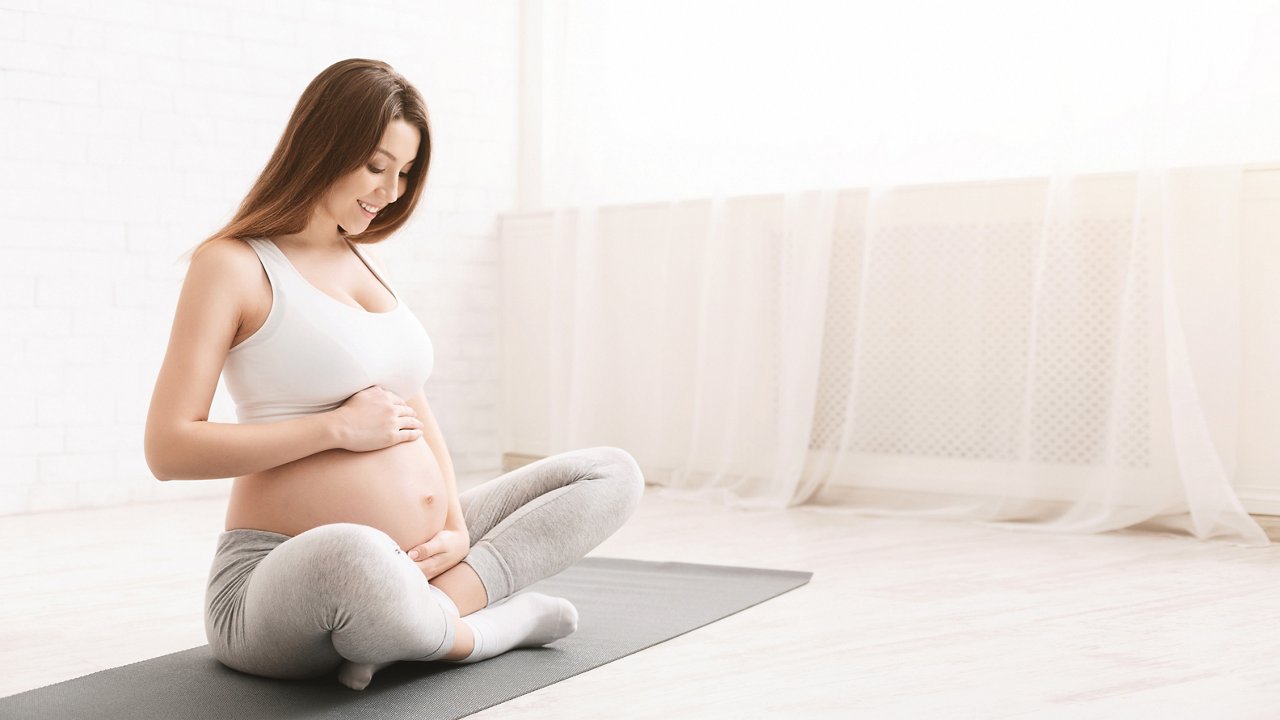 Frau sitzt beim Yoga in der Schwangerschaft im schneidersitz auf einer Yogamatte