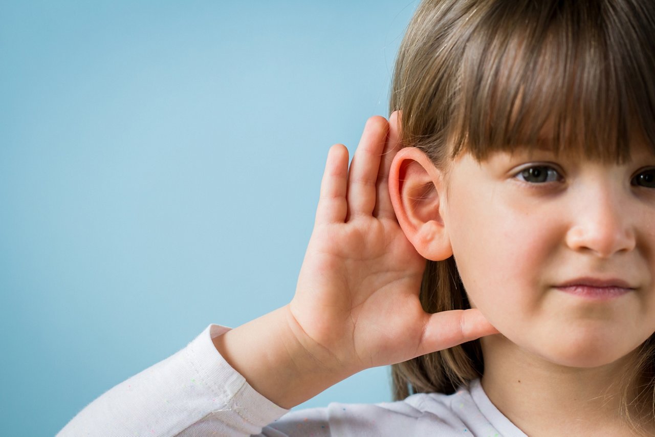 Child with hearing problem on blue background. Hearing loss in childhood, symptoms and treatment concept. Close up, copy space.