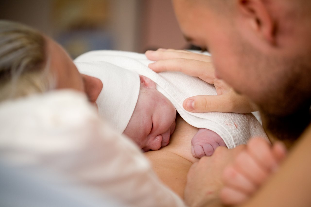 neugeborenes Baby auf der Brust der Mutter mit der Hand des Vaters 