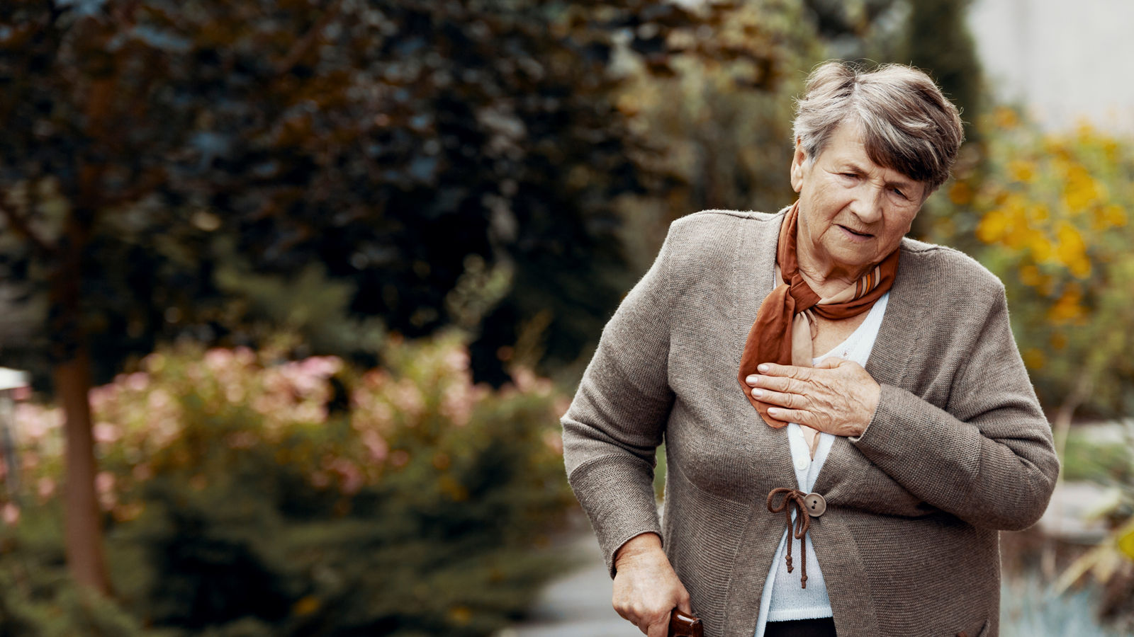 Weak senior woman with walking stick waiting for help during breathlessness attack