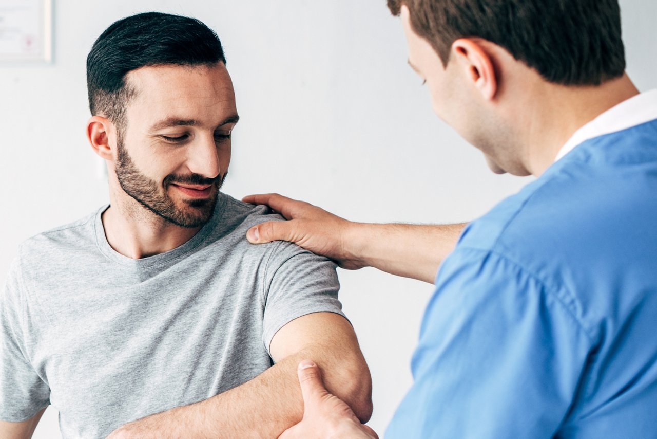 panoramic shot of chiropractor massaging arm of patient in hospital with copy space