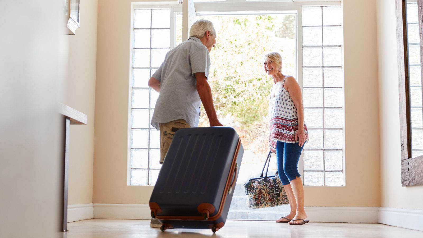 Senior Couple Standing By Front Door With Suitcase About To Leave For Vacation