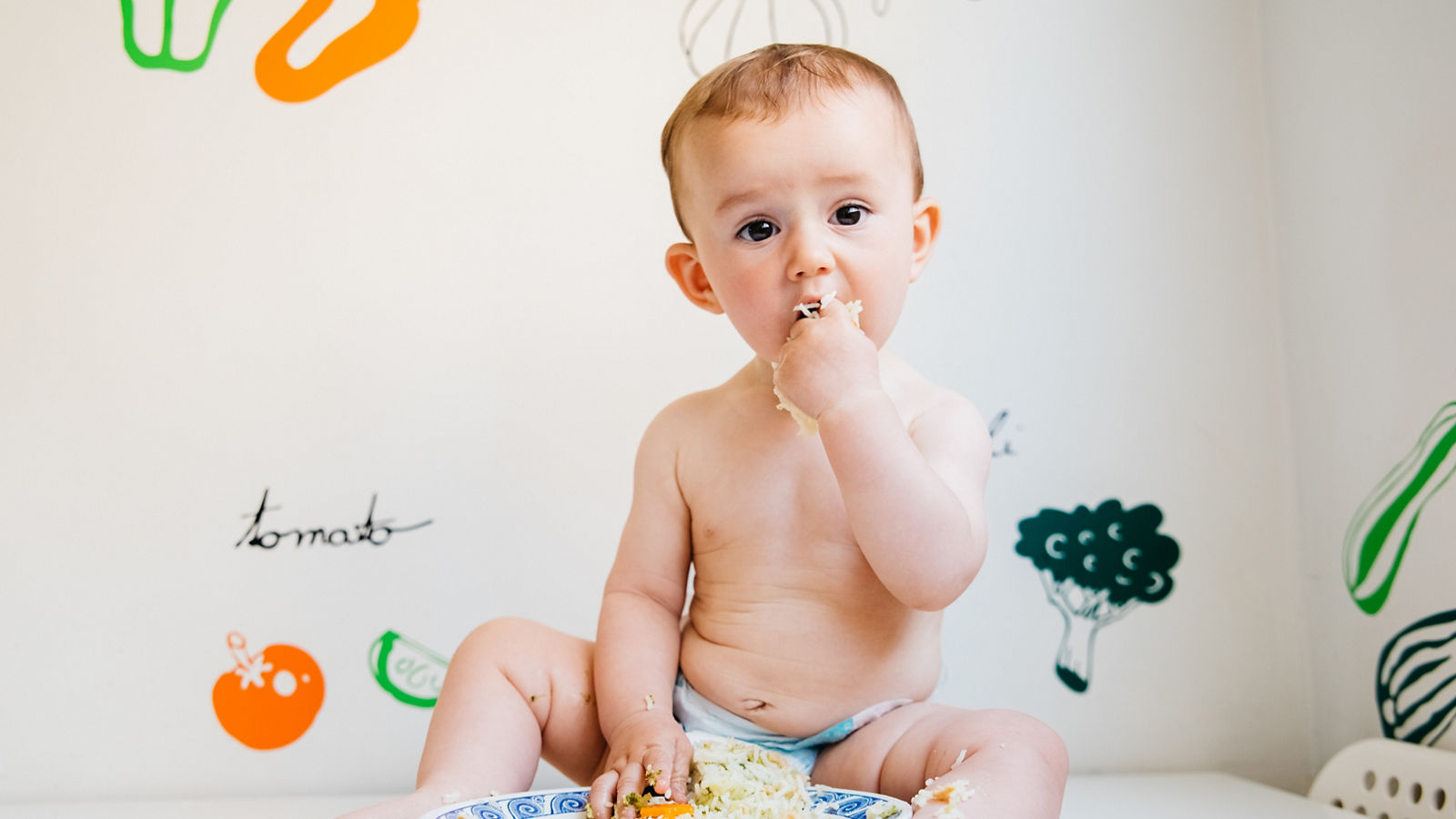 Baby eating by himself learning through the Baby-led Weaning method, exploring the flavors of food with curiosity.