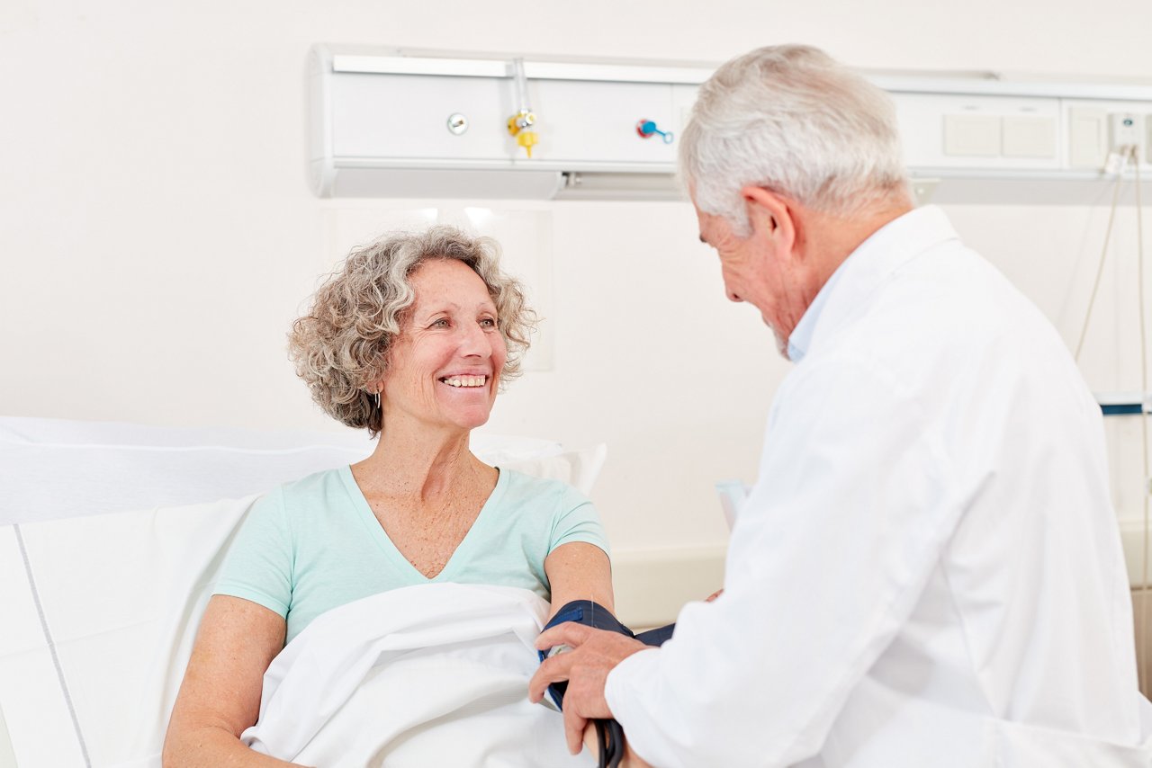 Arzt misst den Blutdruck bei einer lächelnden Senior Frau im Krankenhaus