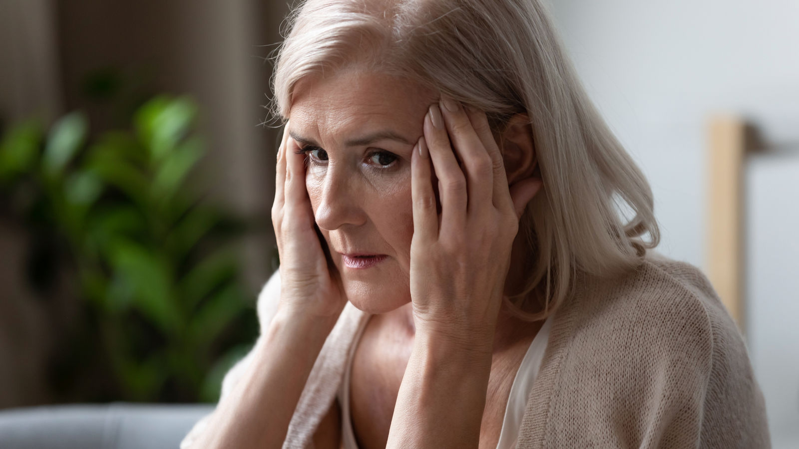 Upset older woman touching temples, feeling bad, pressure, sitting alone, mental disorder or dementia, frustrated mature female looking in distance, thinking about emotional or health problem