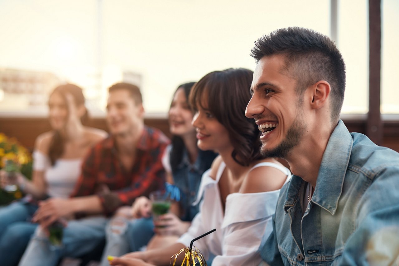 Group of young smiling people drinking cocktails and relaxing on rooftop terrasse at sunset. Friendship concept