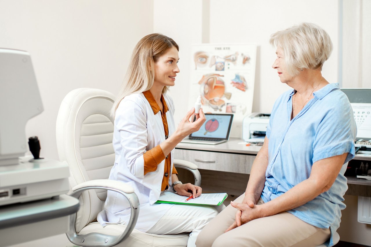 Senior woman patient talking with female ophthalmologist during a medical consultation at the ophthalmologic office. Doctor offering eye medcine for a patient