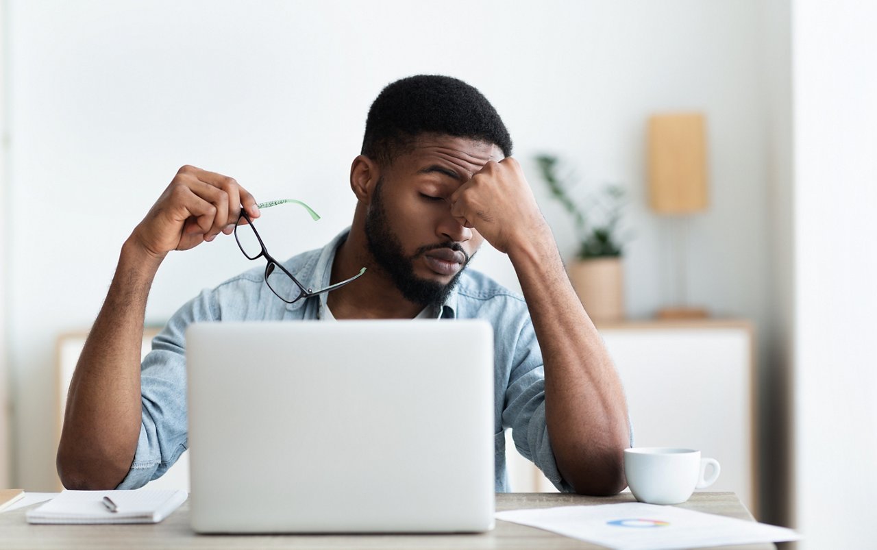 Tired african american employee having headache after working on laptop in office, copy space