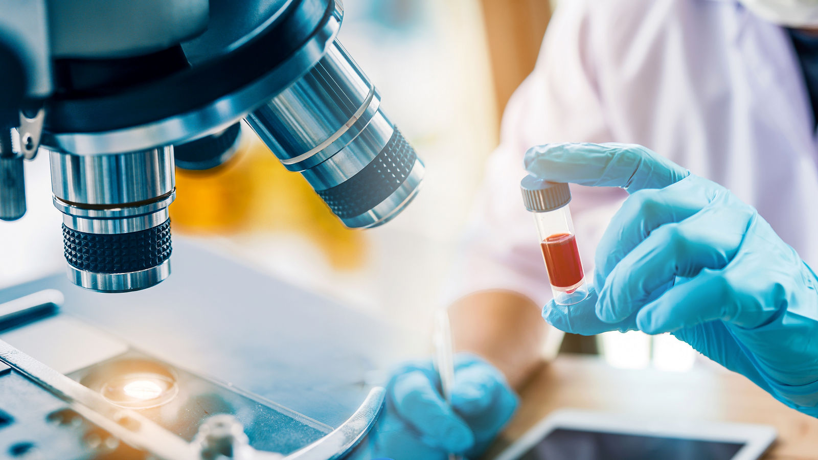 lab technician assistant analyzing a blood sample in test tube at laboratory with microscope. Medical, pharmaceutical and scientific research and development concept.