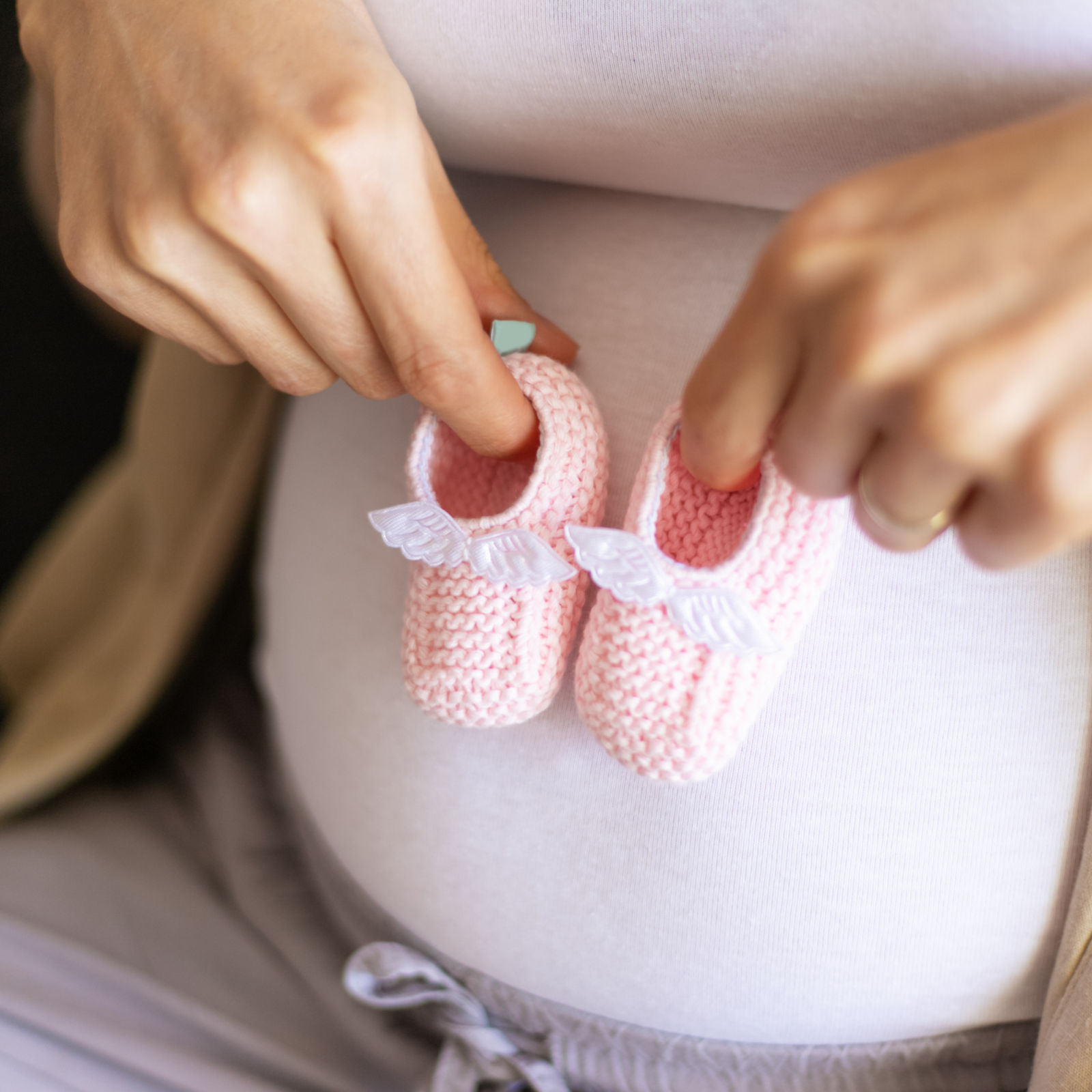 Schwangere Frau hält gestrickte Baby-Schuhe vor ihrem Bauch