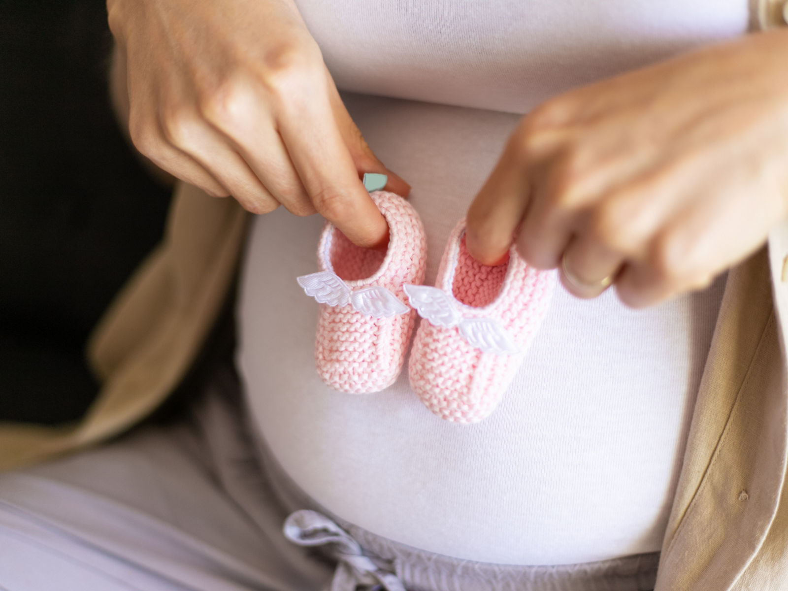Schwangere Frau hält gestrickte Baby-Schuhe vor ihrem Bauch