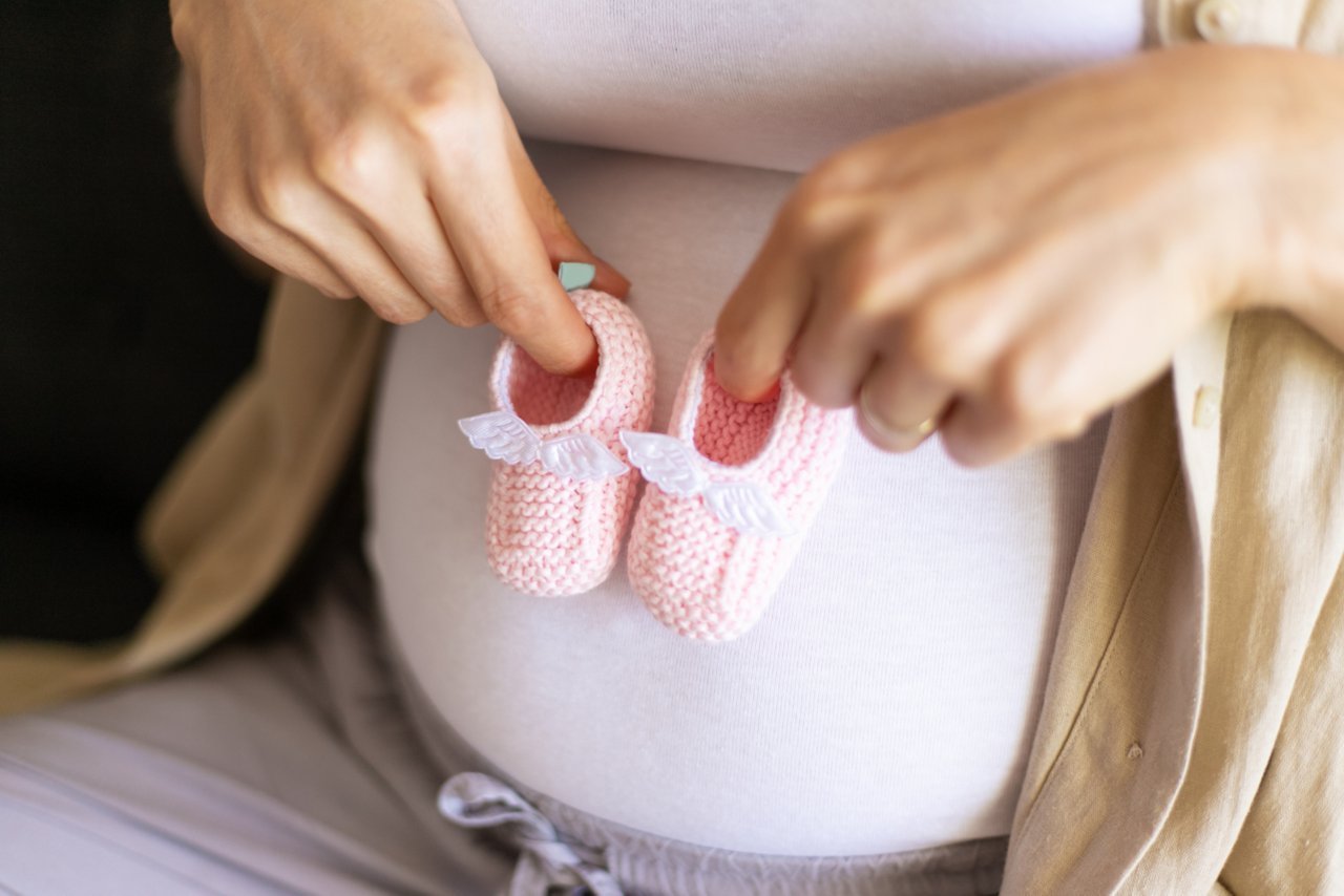 Schwangere Frau hält gestrickte Baby-Schuhe vor ihrem Bauch