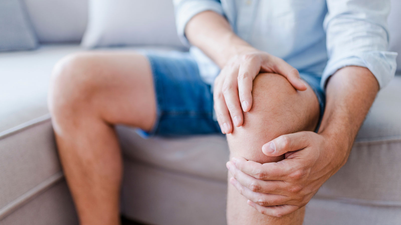 Man suffering from knee pain sitting sofa
