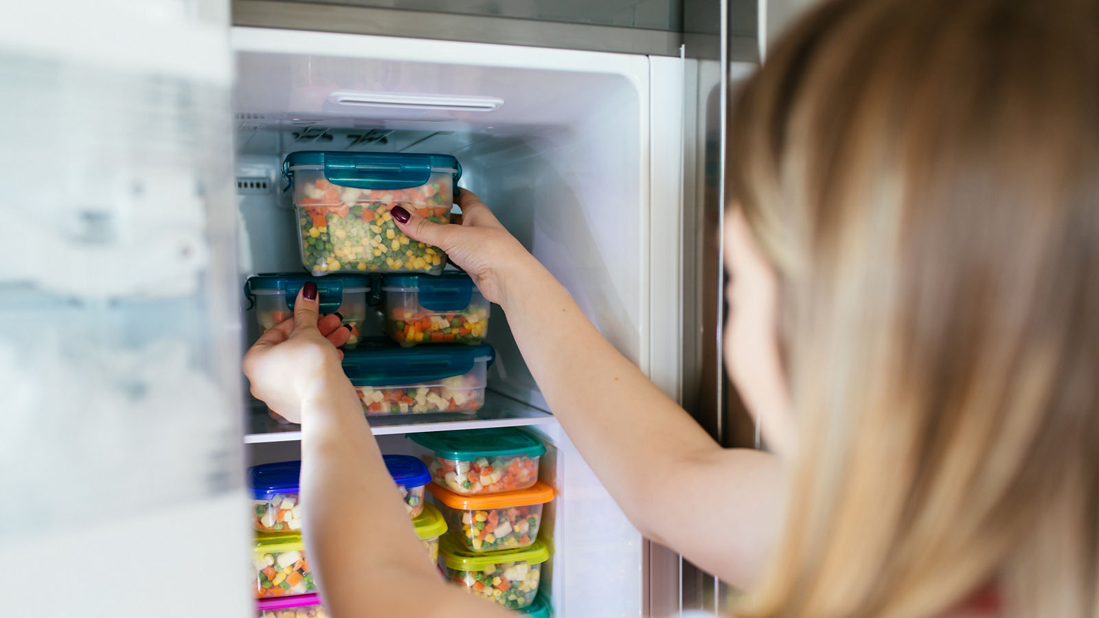 Woman placing container with frozen mixed vegetables in freezer.