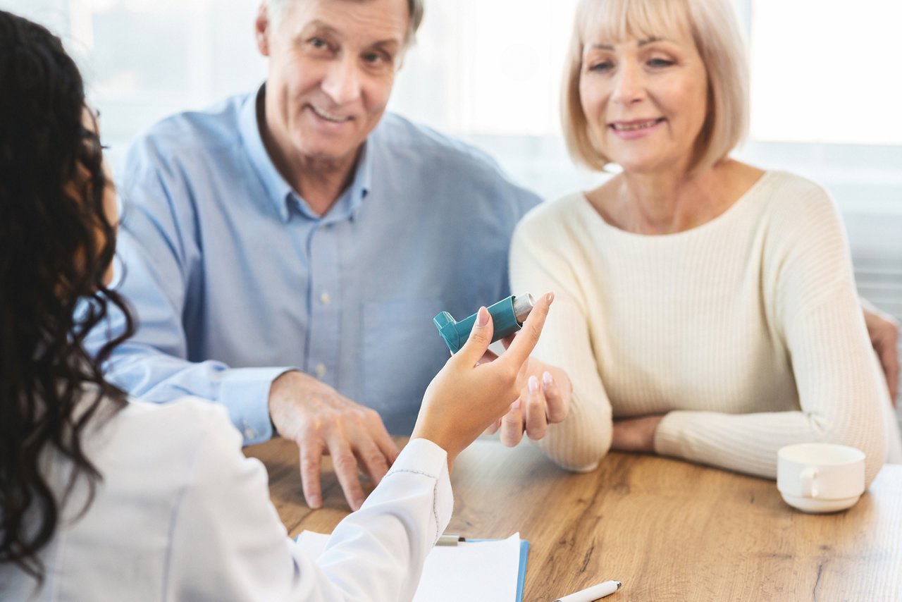 Asthma Attacks. Unrecognizable nurse giving blue inhaler to smiling mature couple, selective focus