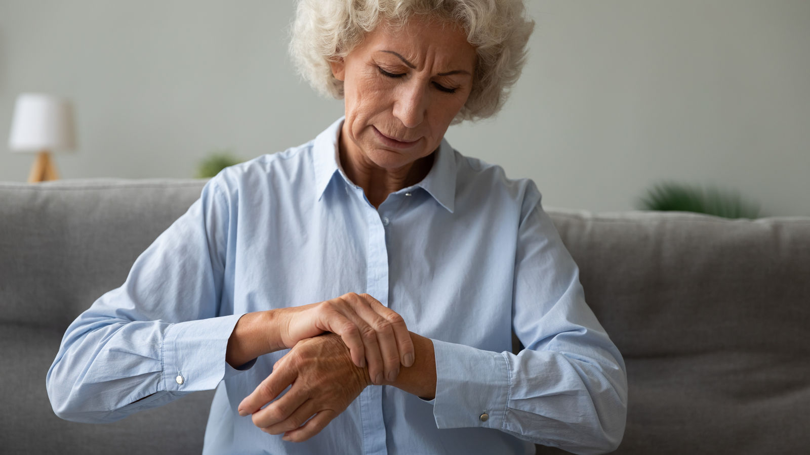 Unhappy older woman massaging wrist, feeling pain in joint, upset mature female sitting on couch alone, health problem concept, rheumatism, arthritis and osteoarthritis concept, chronic disease