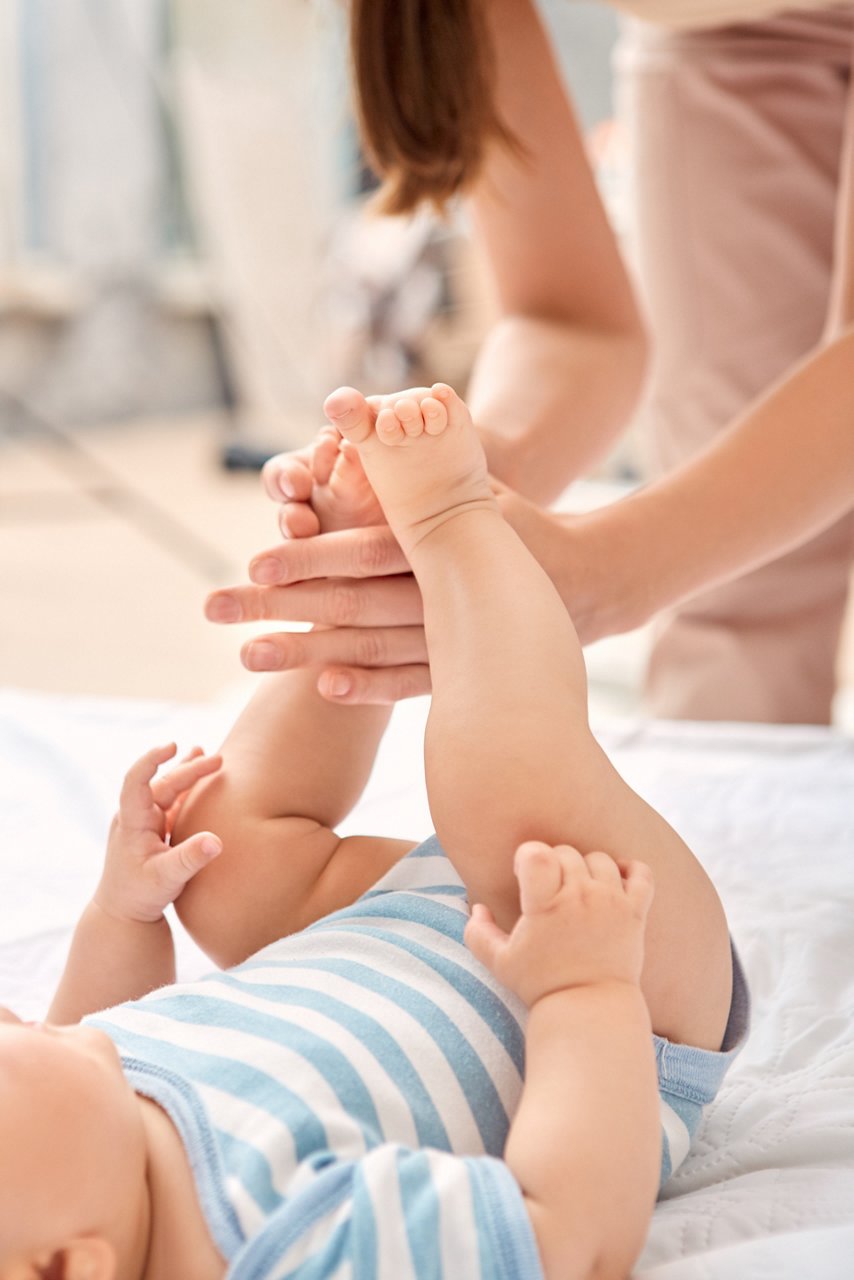 Vertical and cropped view of tender and young adult woman making gentle massage to her little new born baby in bedroom on cozy bed
