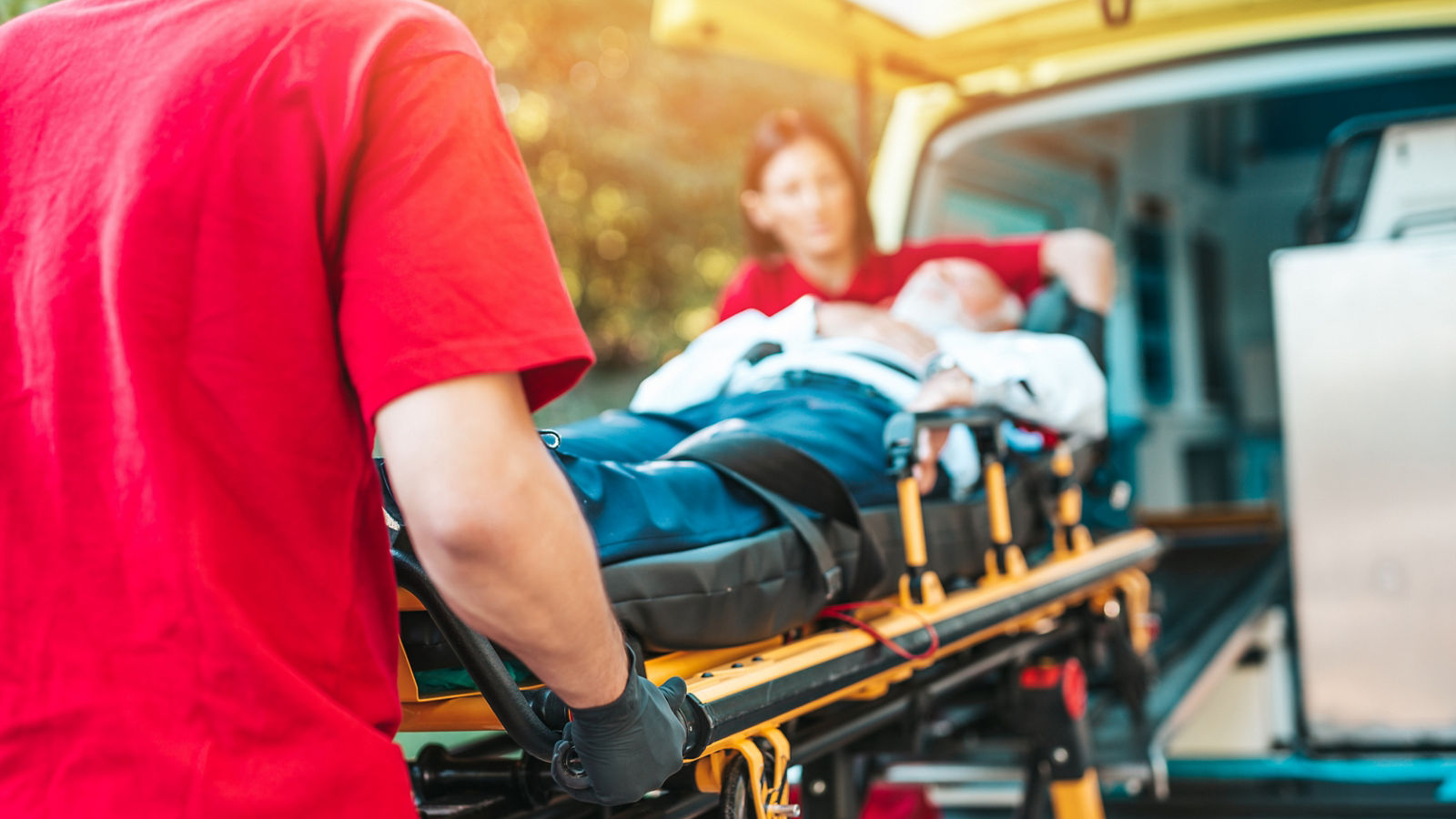 Emergency medical service at work. Paramedic is pulling stretcher with senior man with serious heart attack to the ambulance car. Help on the road. Drivers assistance concept.