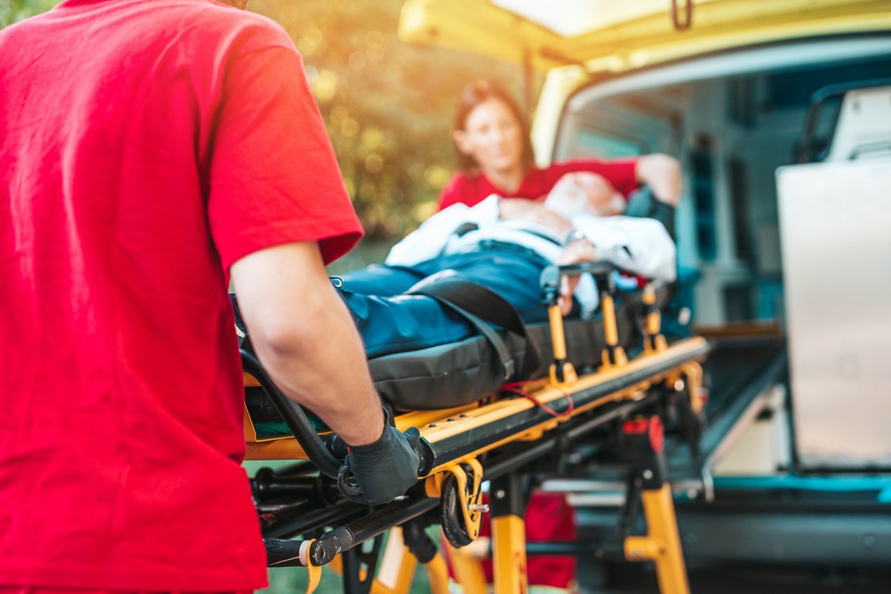 Emergency medical service at work. Paramedic is pulling stretcher with senior man with serious heart attack to the ambulance car. Help on the road. Drivers assistance concept.