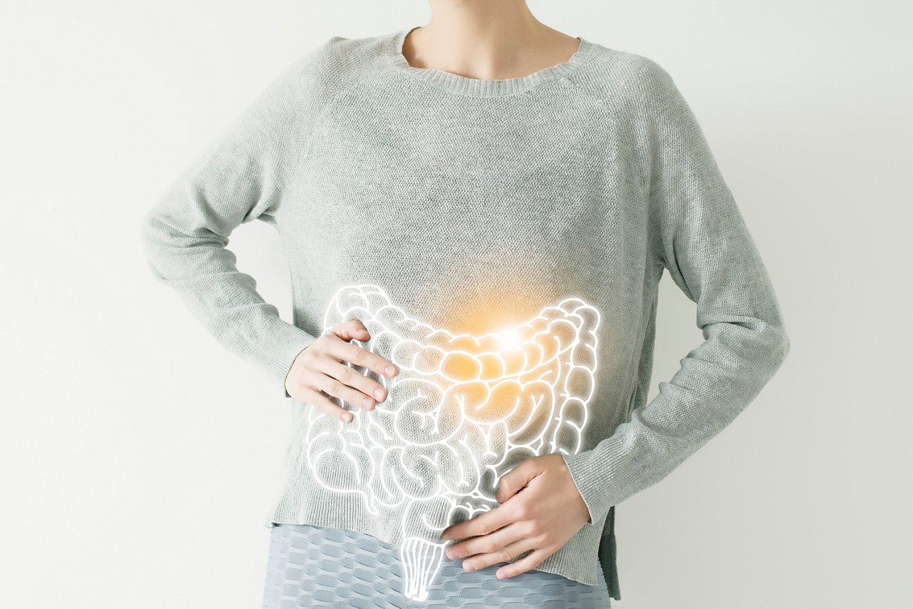 Frau in grauem Pulli hält Bauch mit eingezeichnetem Darm