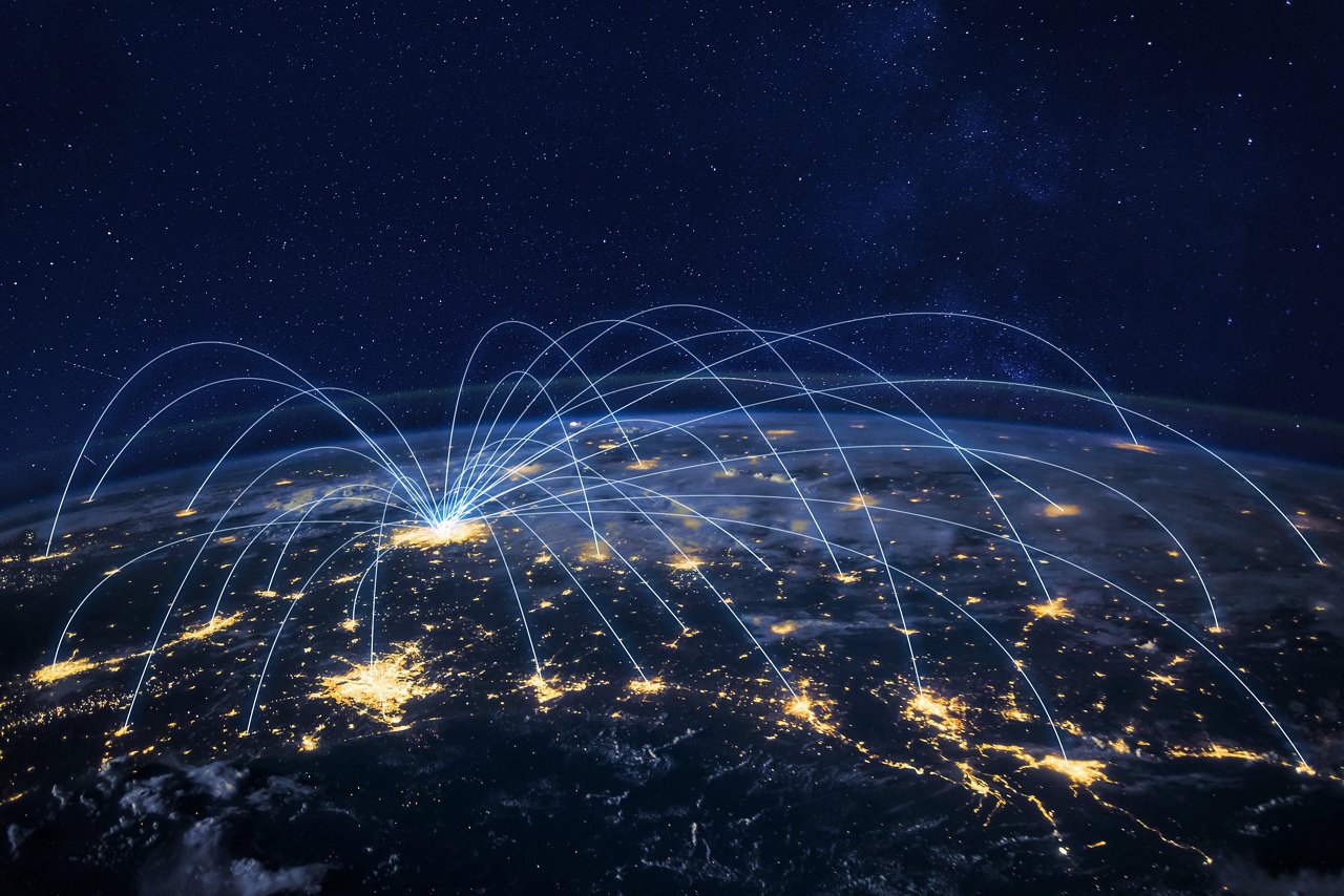 Darstellung der Erdoberfläche bei Nacht mit vielen hell erleuchteten Städten, die über weißblaue Lichtbögen mit einem zentralen Punkt verbunden sind, Darstellung eines Hub-and-spoke Netzwerks.