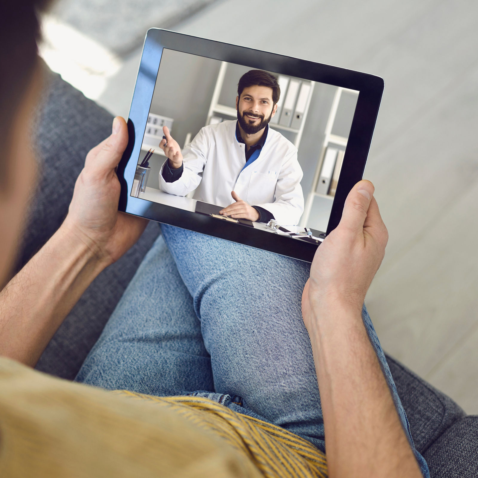 Online medical consultation for patients. Doctor man video call using laptop talks with male patient sitting on the sofa at home. Telemedicine concept virtual hospital medicine diagnosis symptoms prescription.