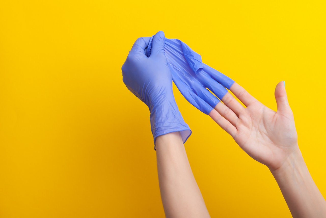 Ein bleuer unsteriler Gummihandschuh wird von der Hand abgestreift 