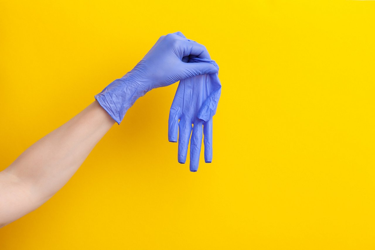 Ein blauer unsteriler Einweghandschuh wird von einer Hand festgehalten, die noch einen zweiten blauen Handschuh trägt