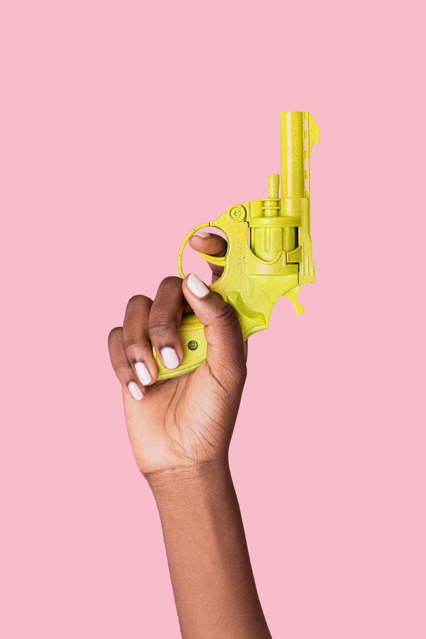 Gelbe Spielzeugpistole aus Plastik in einer Hand mit Finger am Abzug