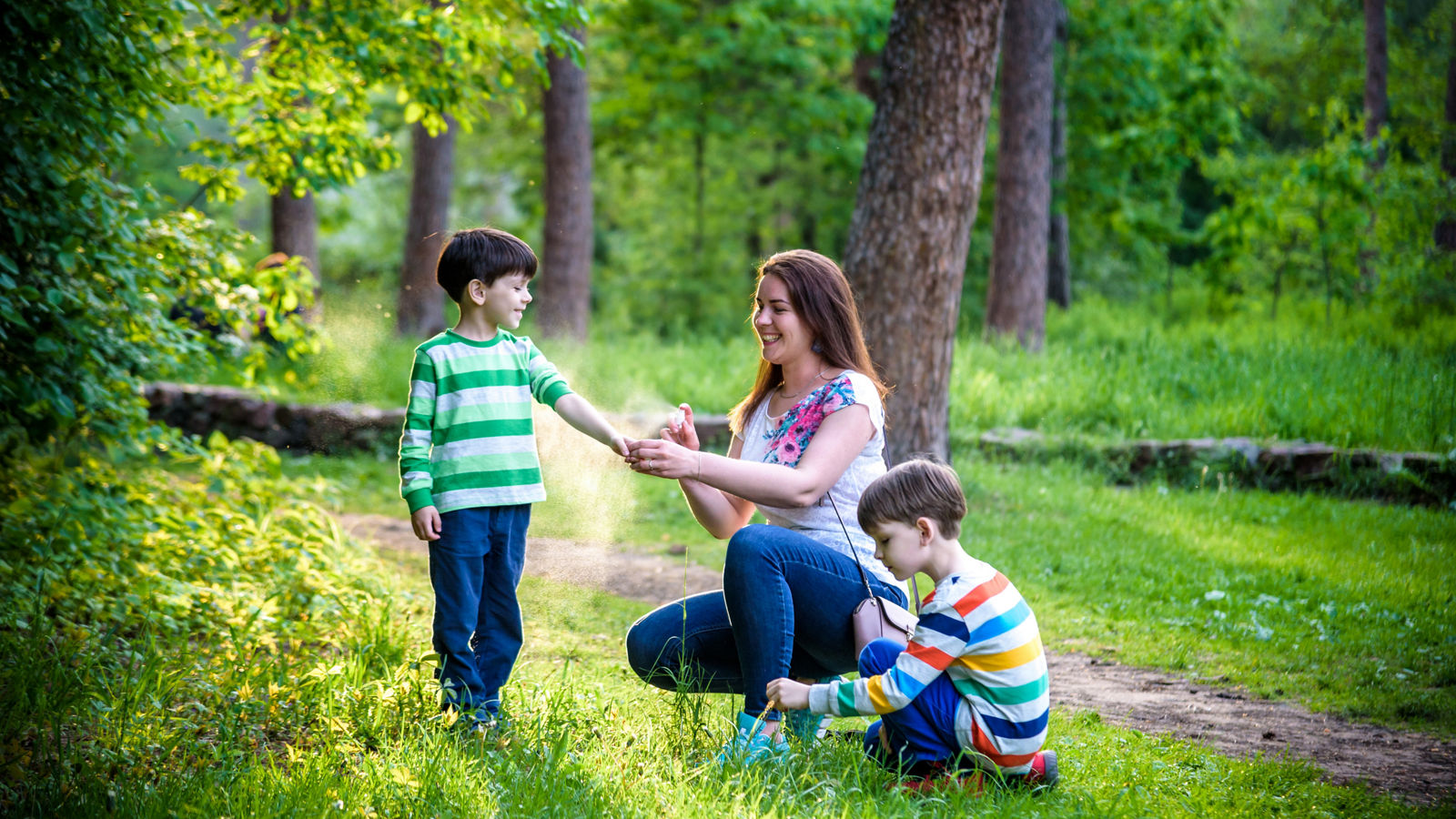 Young woman mother applying insect repellent to her two son before forest hike beautiful summer day or evening. Protecting children from biting insects at summer. Active leisure with kids