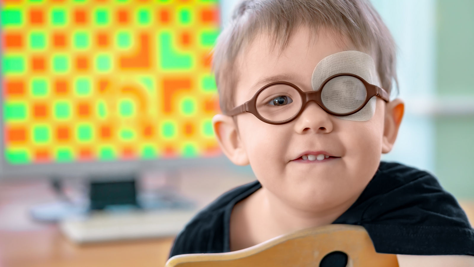 A little boy wearing glasses and an eye patch (plaster, occluder). Apes or grimaces. He undergoes vision treatment to prevent amblyopia and strabismus (squint, lazy eye). Child congenital vision disease problem.