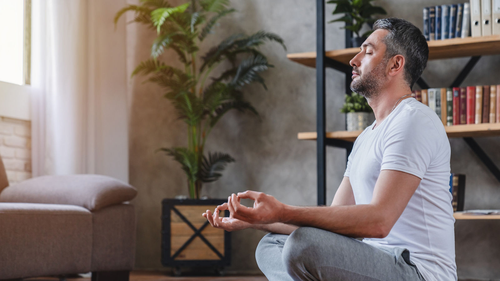 Meditation concept. Calm man meditating while sitting in lotus position relaxing doing yoga at home