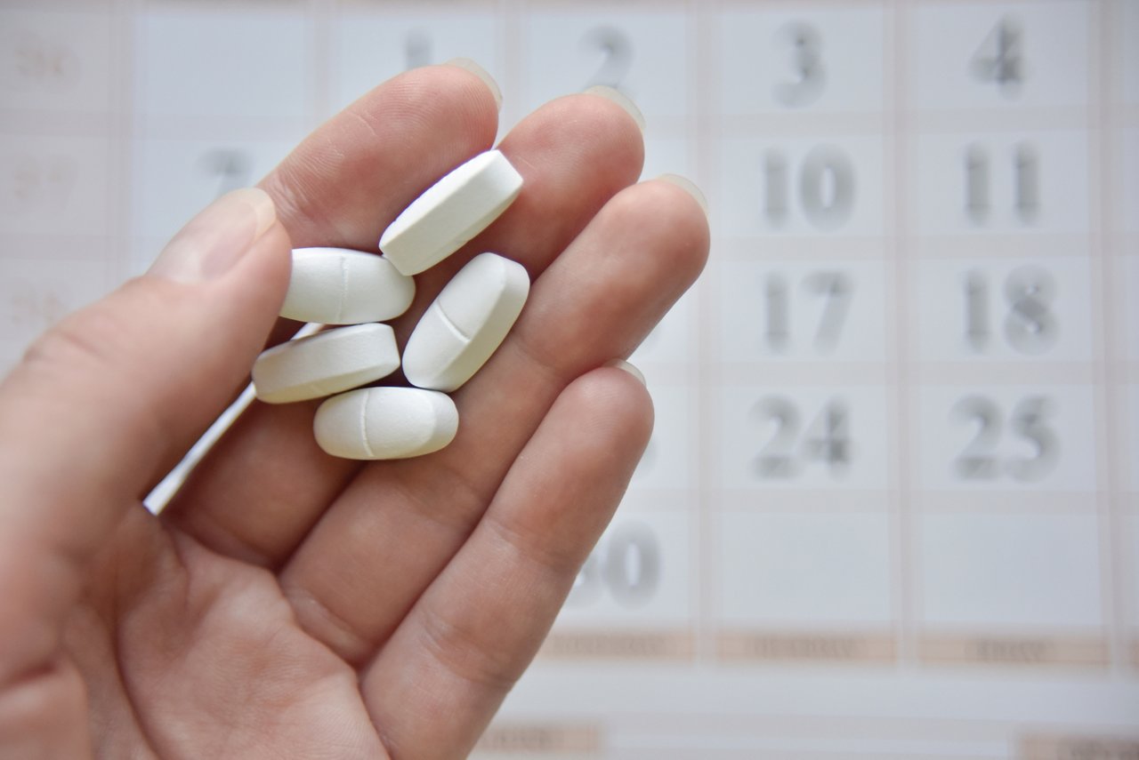 selective focus at the hand and pills with the blurred calendar at the background. scheduled treatment concept