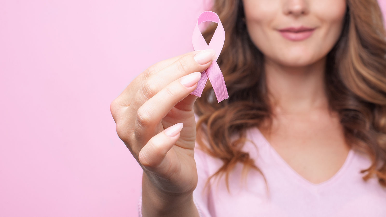 Woman in pink sweater with pink ribbon supporting breast cancer awareness campaign