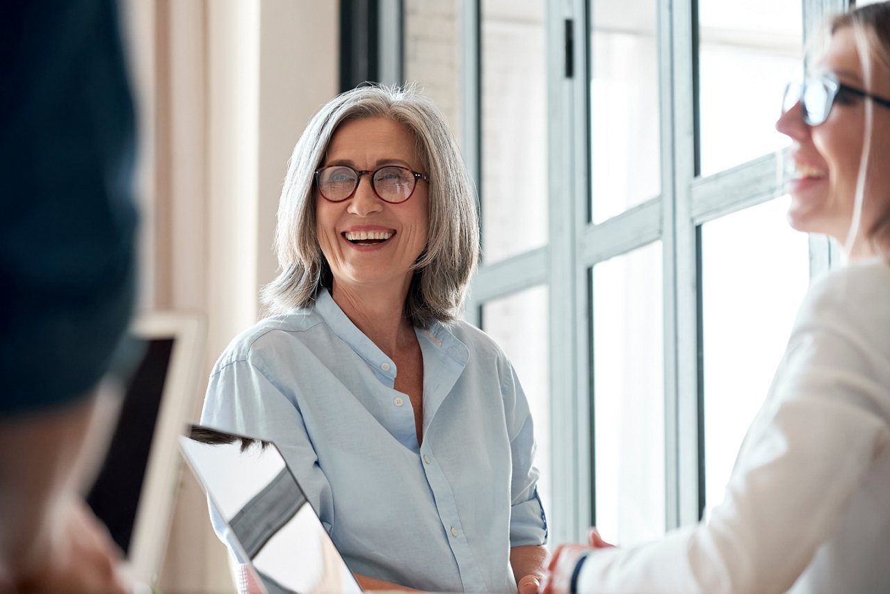 Happy mature old female mentor coach supervisor training young interns at group office meeting professional workshop. Smiling middle aged teacher professor laughing with students at university class