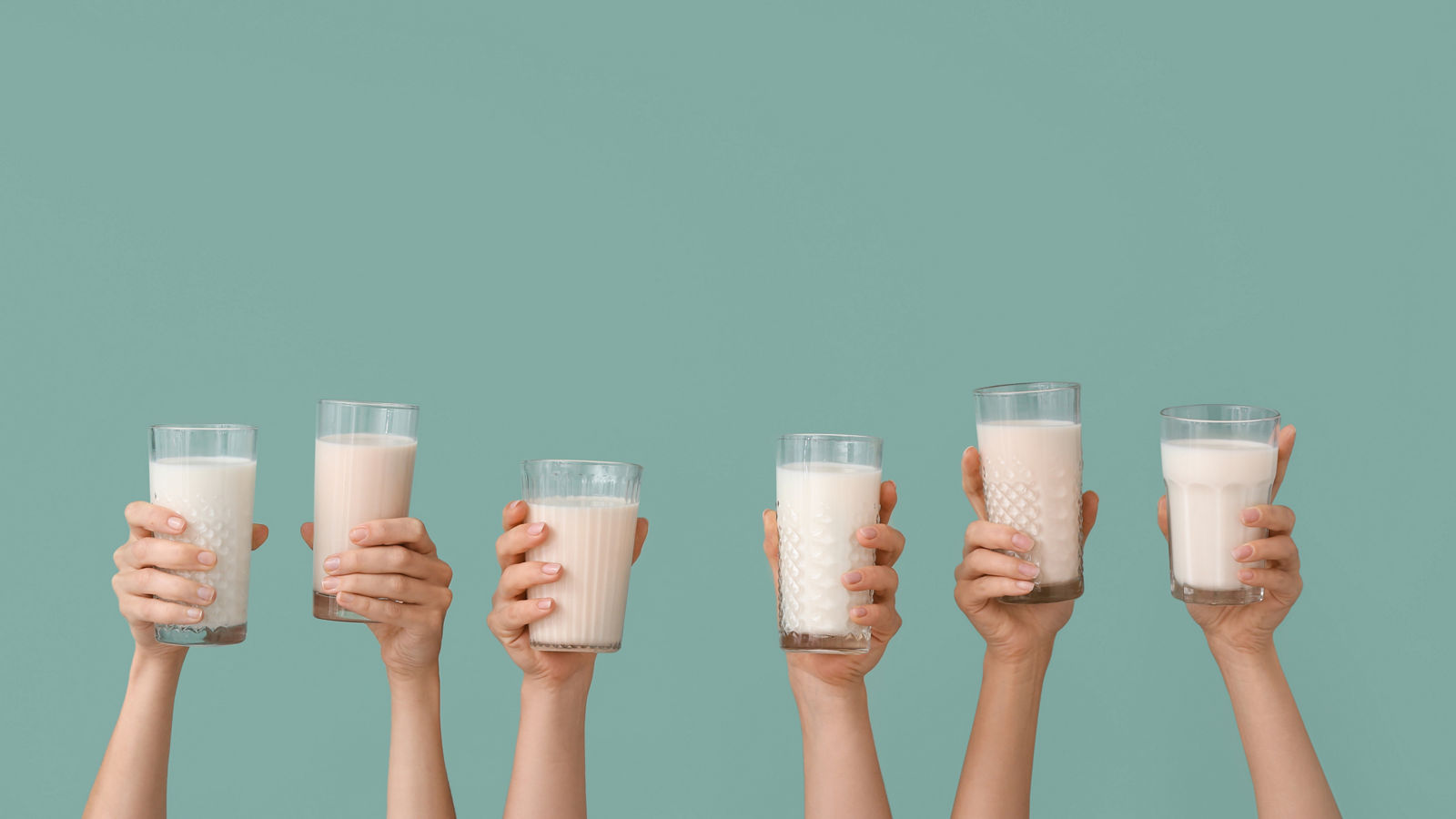 Female hands with glasses of vegan milk on color background
