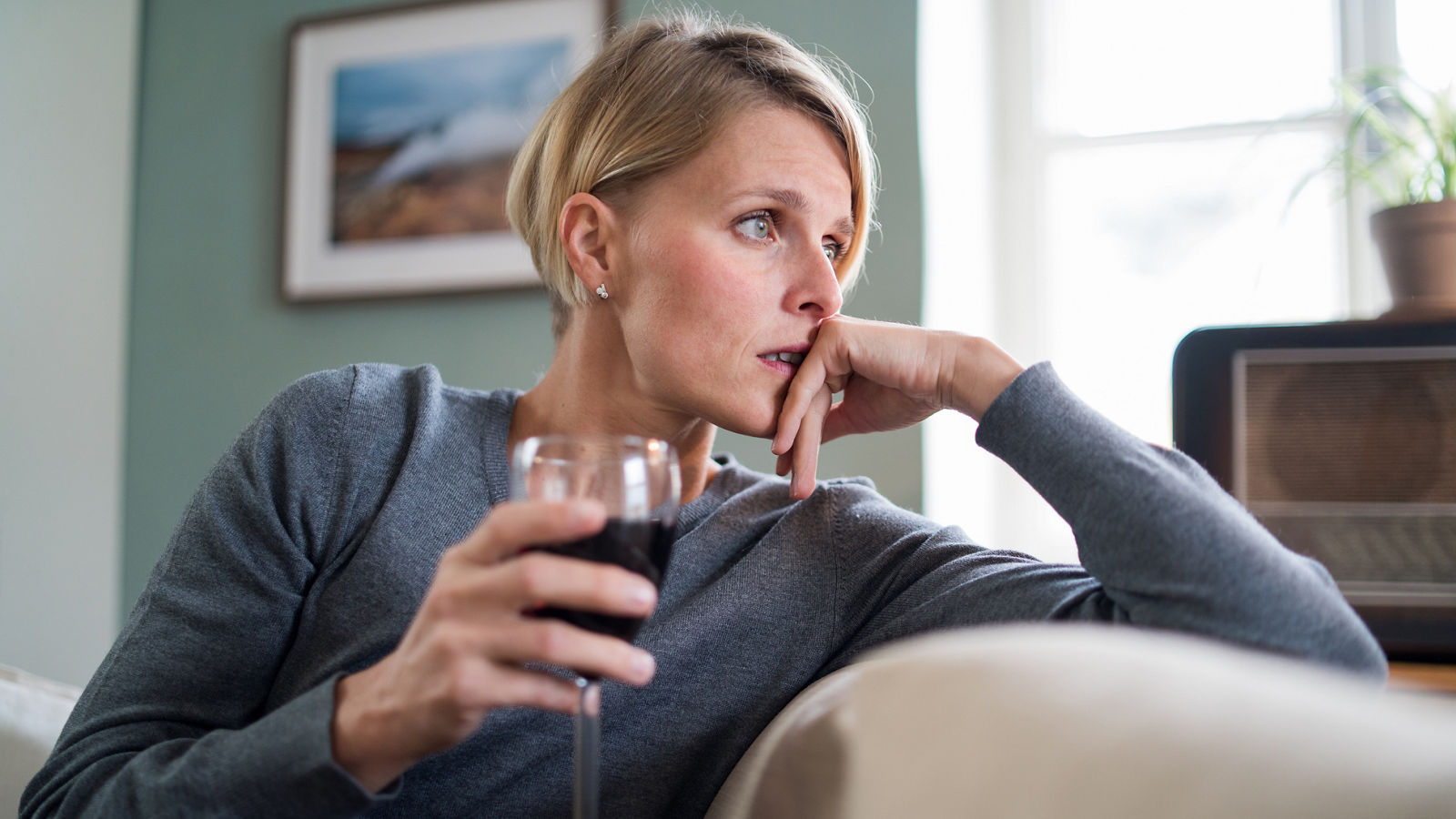 Depressed woman with wine indoors at home, mental health and alcohol addiction concept.