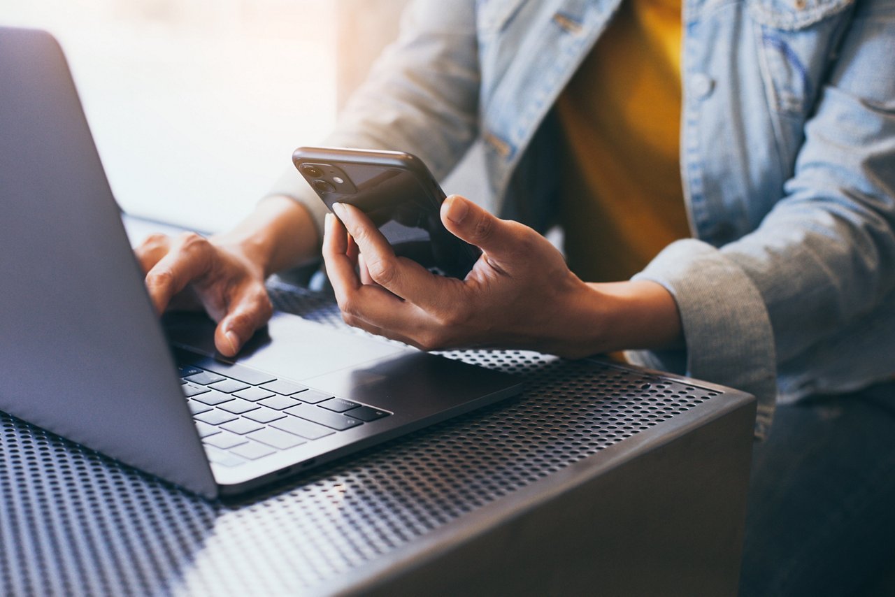 Person sitzt mit Smartphone an einem Laptop