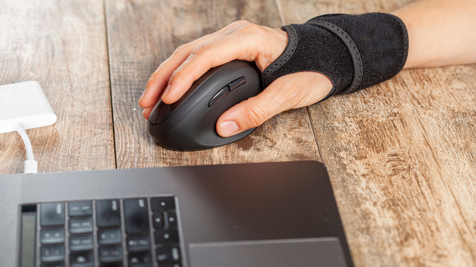 Chronic trauma to the wrist joint  in people using computer mouse may lead to disorders that cause inflammation and pain. A woman working on desk uses wrist support brace and ergonomic vertical mouse,Chronic trauma to the wrist joint  in people using computer mous