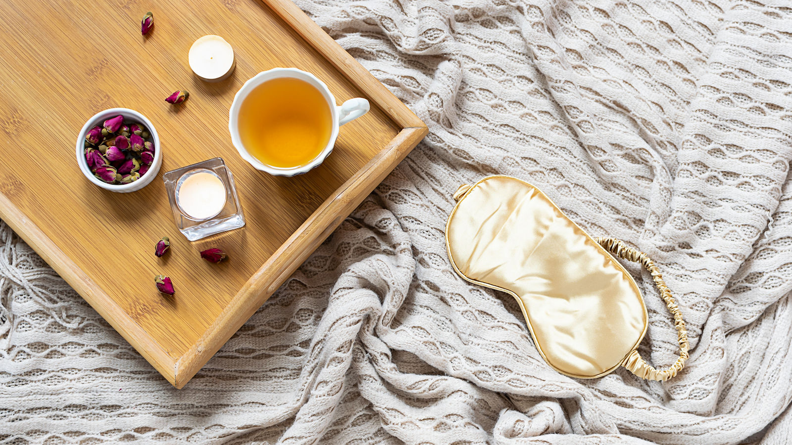 Cozy home interior with warm blanket. herbal tea, aromatic candles and rose buds. Hygge style composition. Sleep optimization concept.