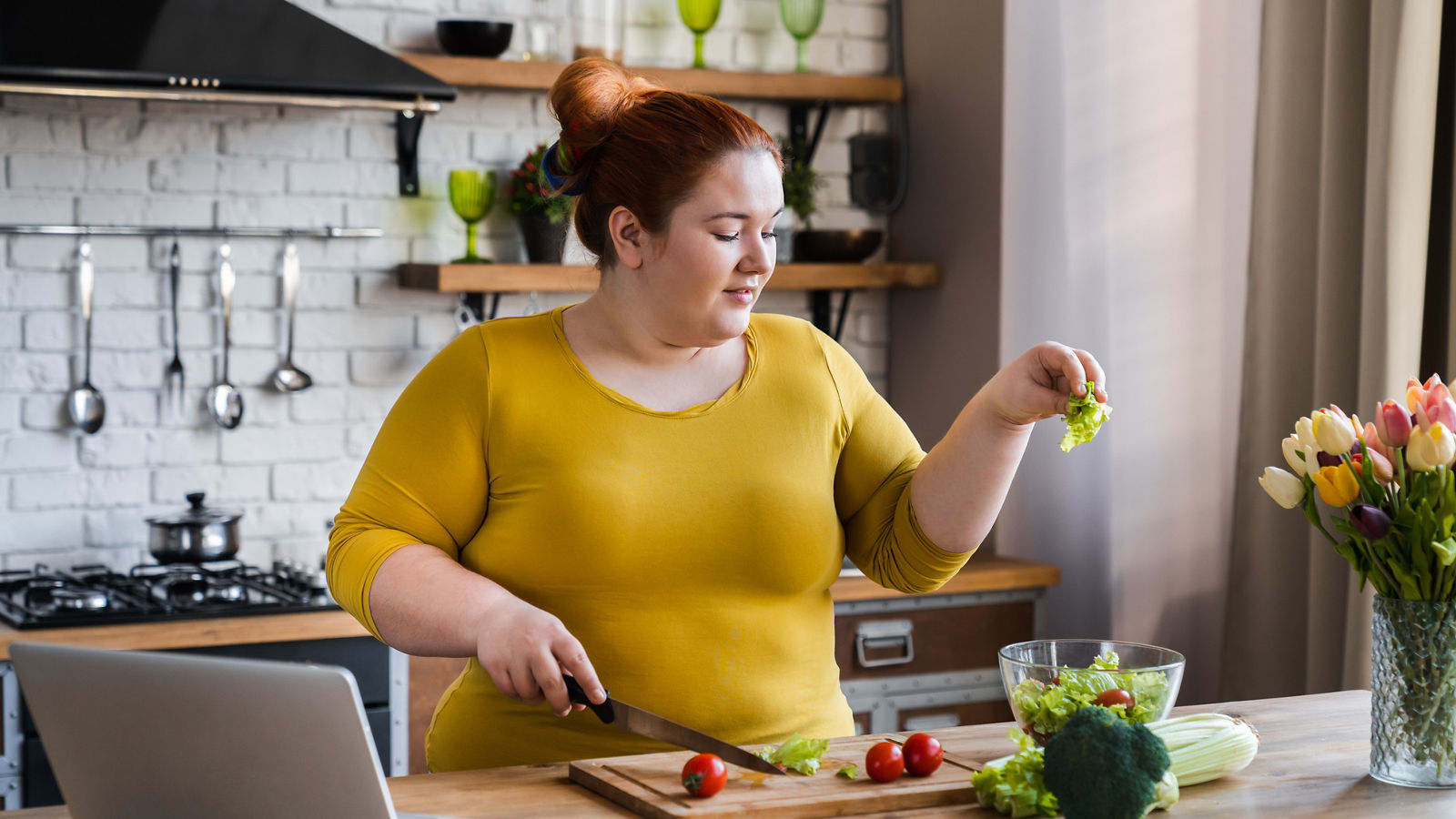 Plus size , fat caucasian woman learning to make salad and healthy food from social media adding vegetables to salad bowl ,Social distancing, stay at home concept,Plus size , fat caucasian woman learning to make salad and healt