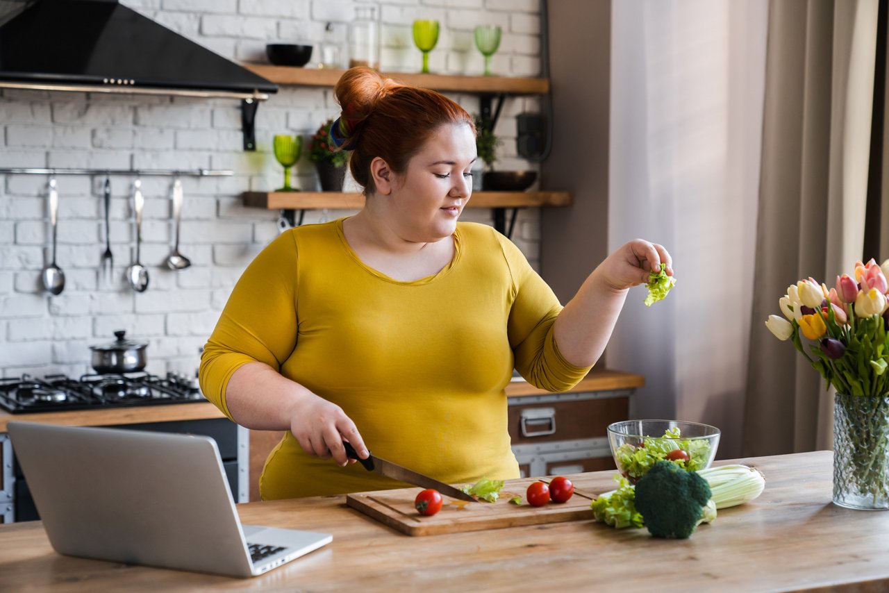 Plus size , fat caucasian woman learning to make salad and healthy food from social media adding vegetables to salad bowl ,Social distancing, stay at home concept