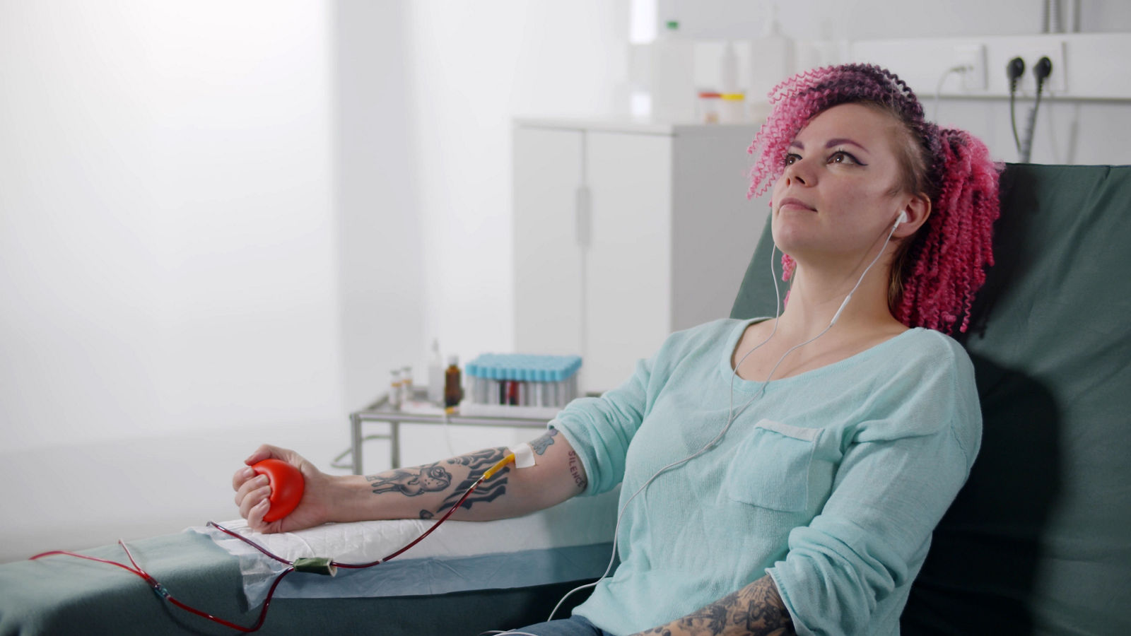 Female patient listening to music while giving her blood in hospital room